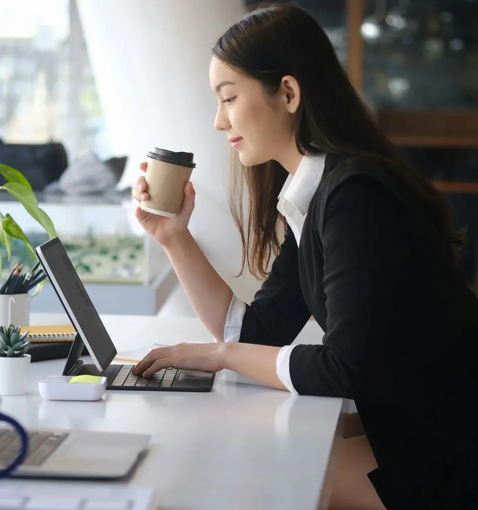 A marketer reviewing work at her desk with a coffee in hand