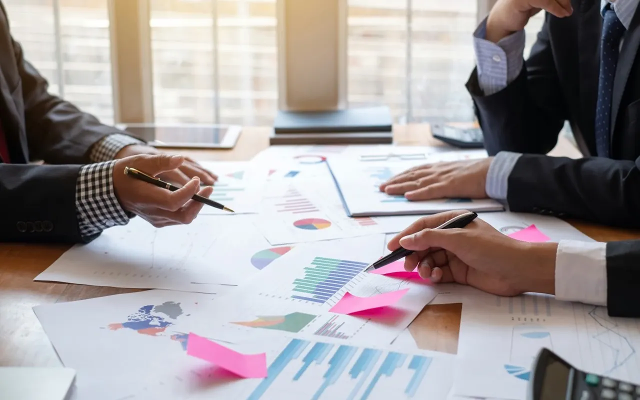 Two consultants reviewing charts and reports spread across a table